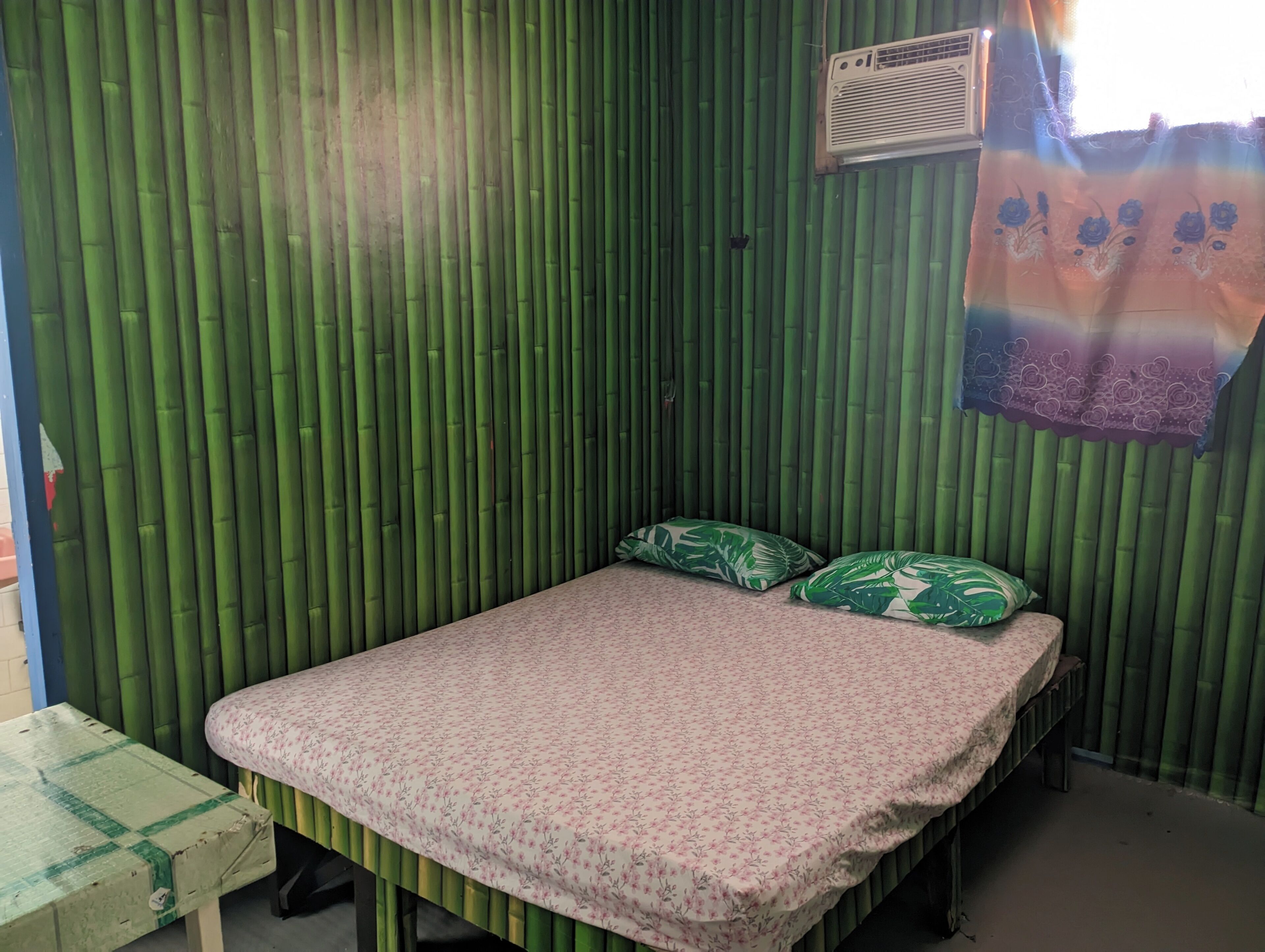 A small room with a bed, a table, and a wall covered in vertical bamboo panels.
