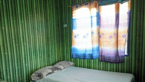 A room with a bed, a window with patterned curtains, and bamboo walls.