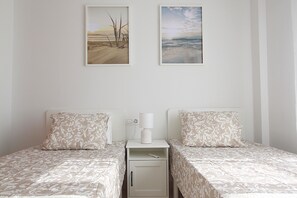 Ein Schlafzimmer mit zwei Betten, jeweils mit gemusterten Bettbezügen, einem Nachttisch mit Lampe und zwei gerahmten Bildern an der Wand.
