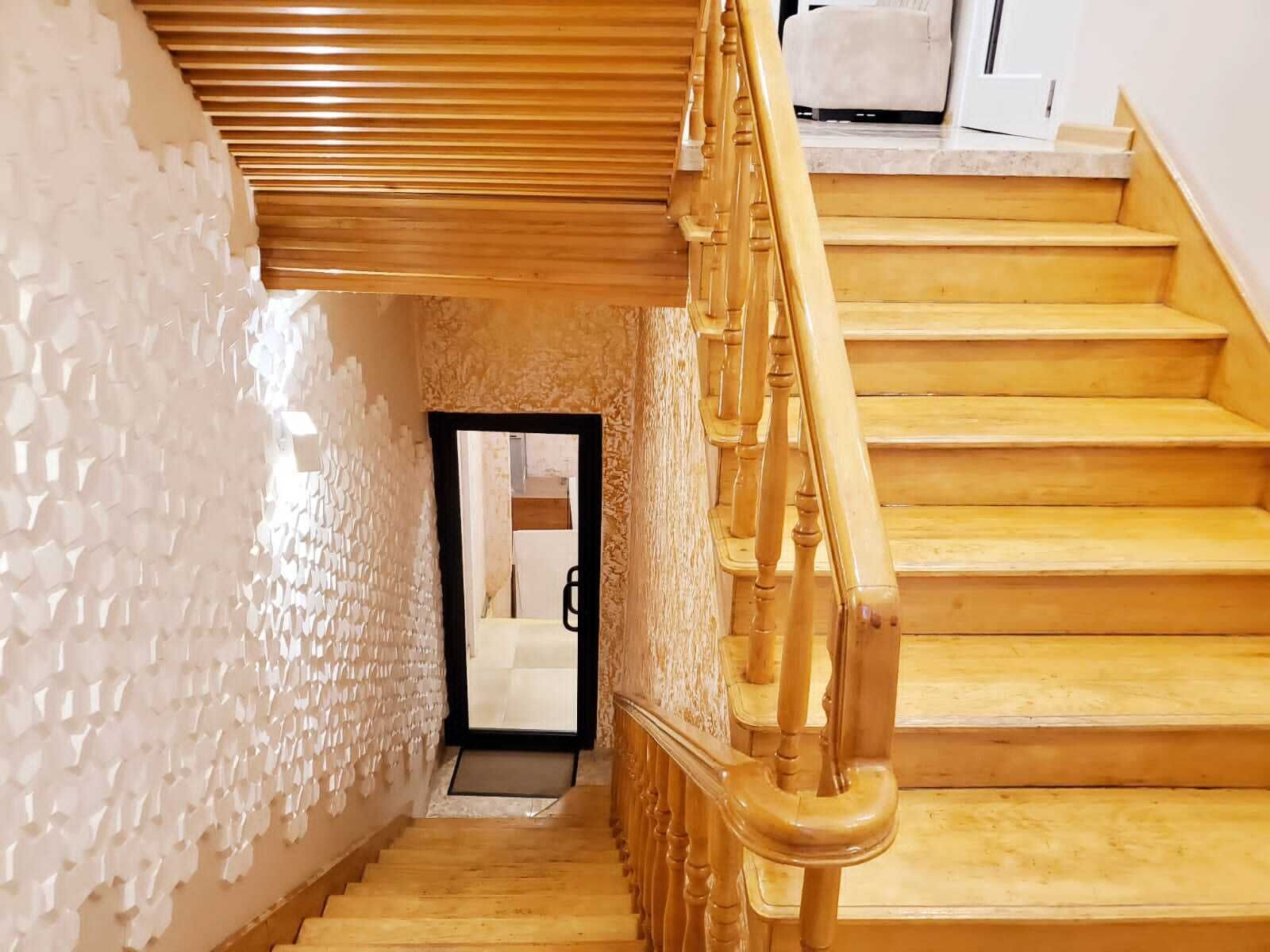 Eine Treppe mit Holzwegen und einem Holzgeländer, die zu einem Raum mit einer weißen, strukturierten Wand und einer Tür führt.