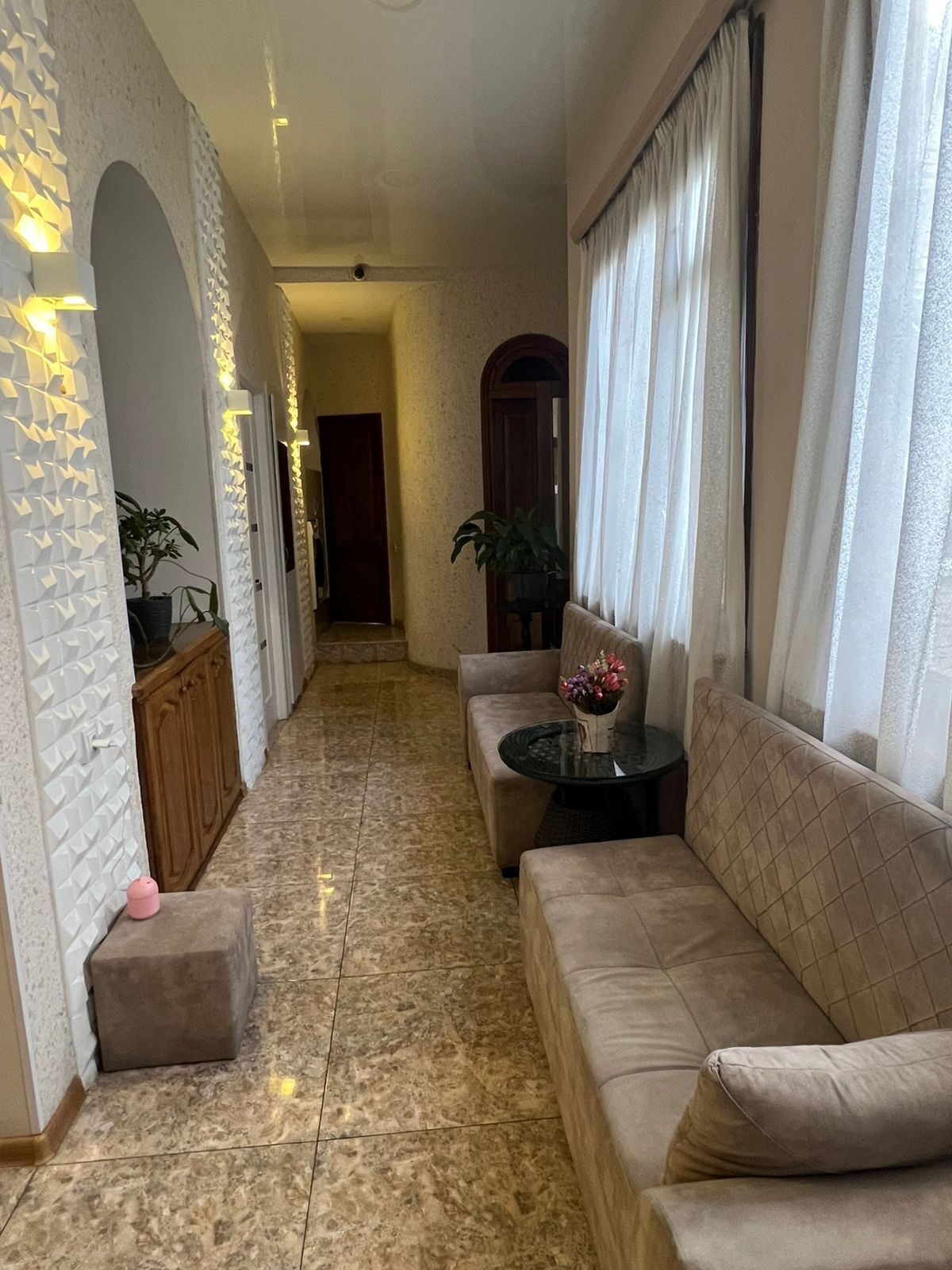 A hallway with a beige sofa, a small table with a vase of flowers, and a potted plant.