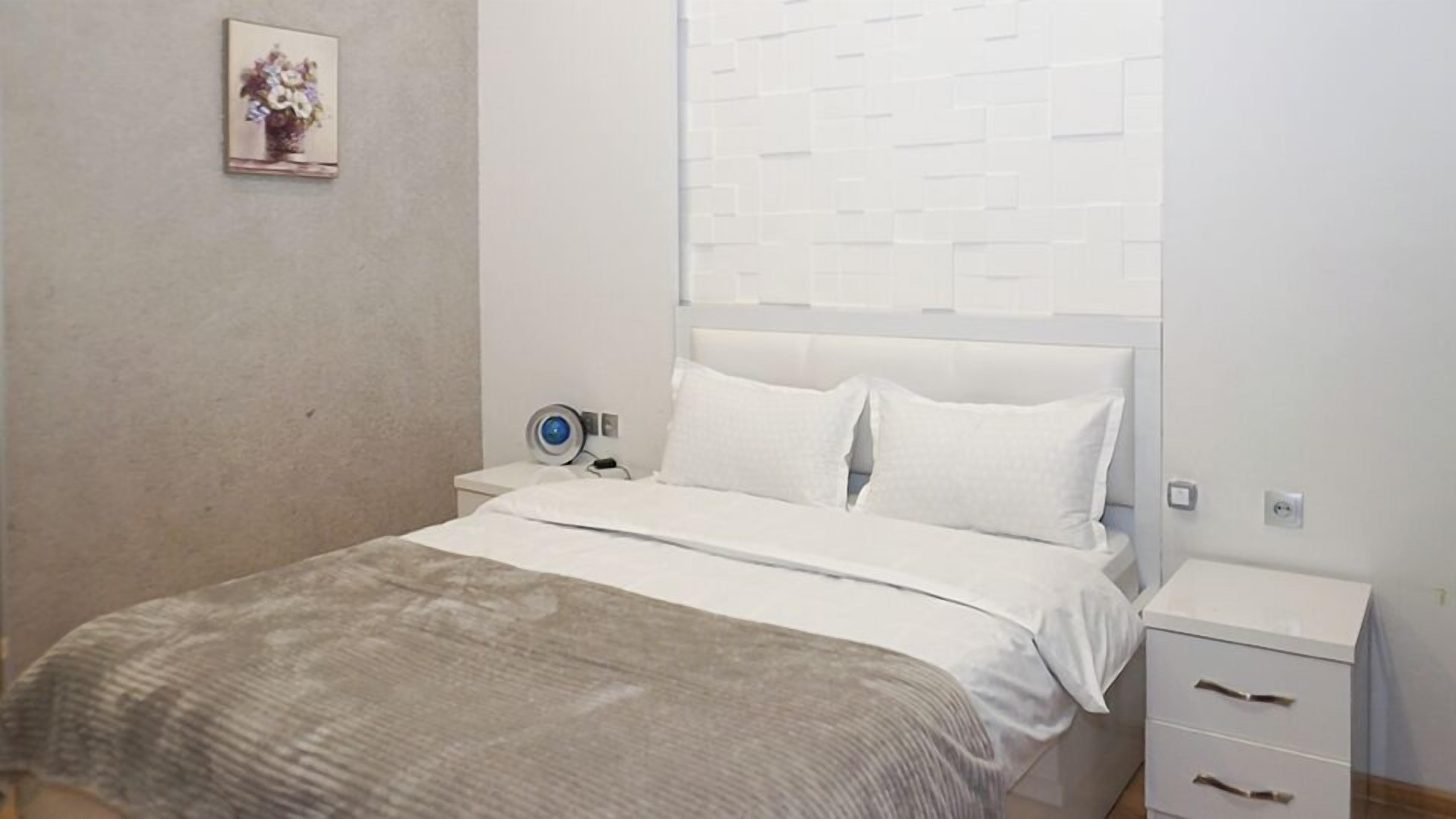 Quarto com cama, mesas de cabeceira e luminária fixada na parede.
