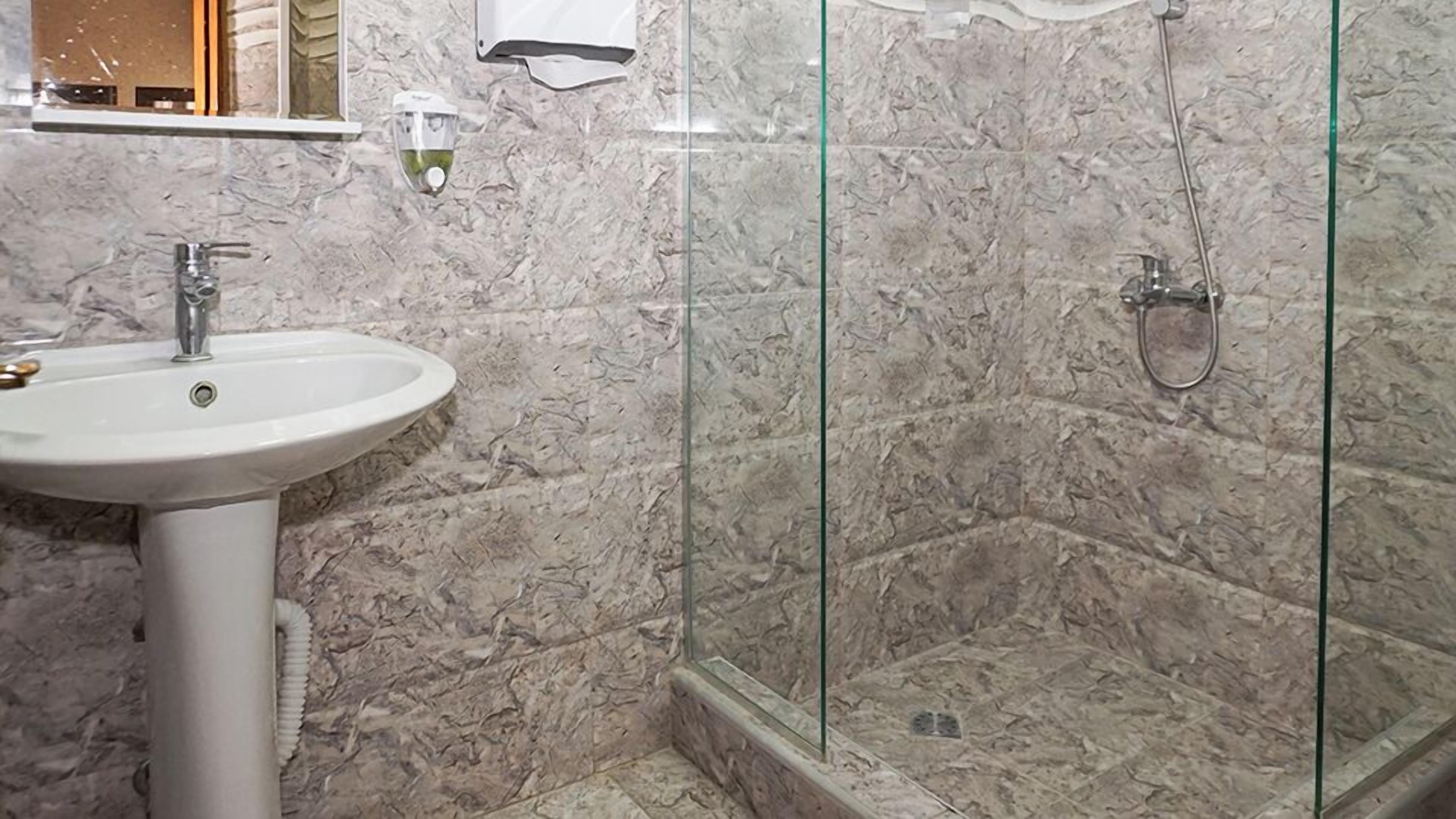A bathroom with a white sink, a glass shower enclosure, and marble walls.