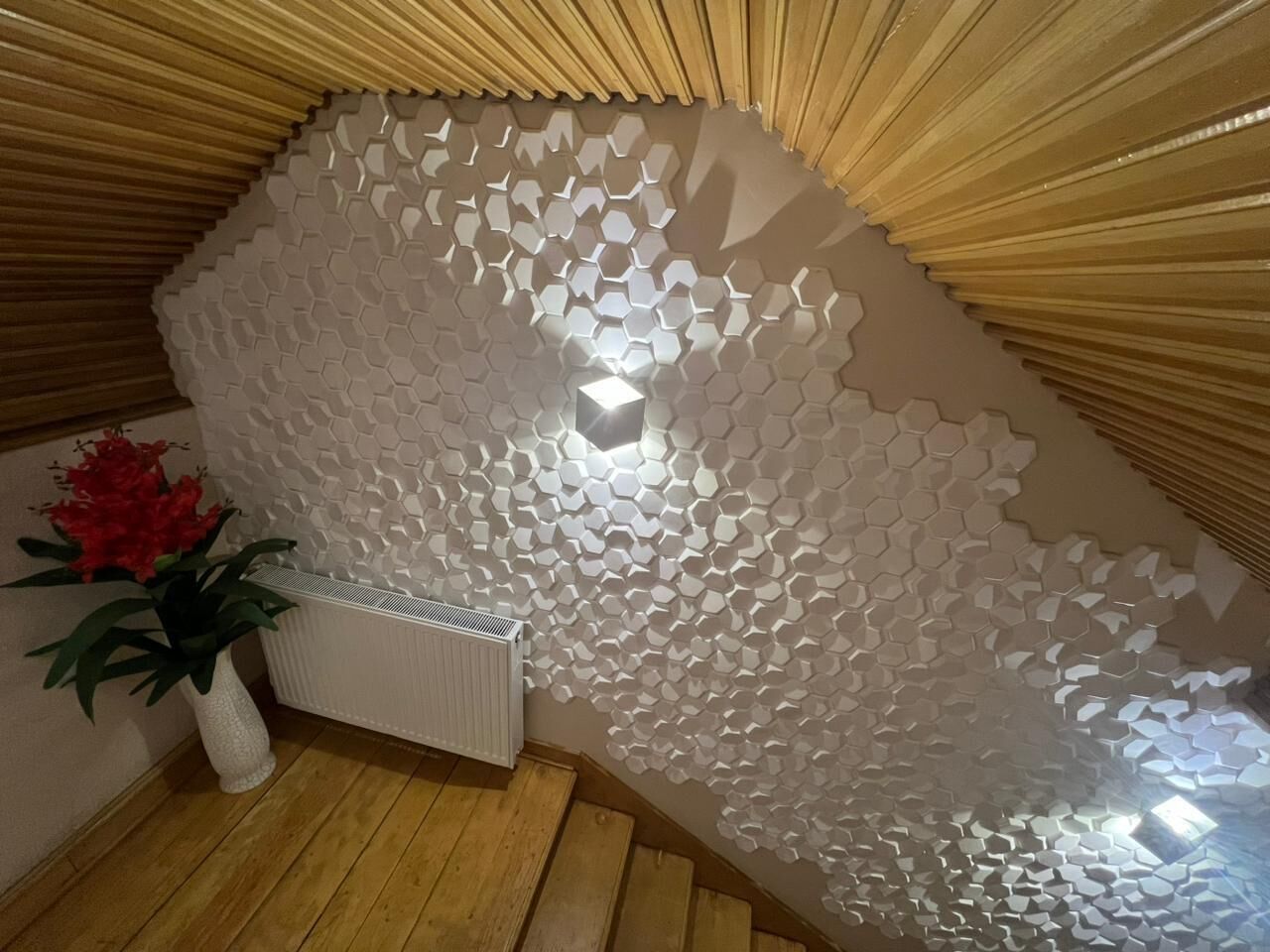 A room with a wooden sloped ceiling, a white radiator, and a wall with a honeycomb pattern.