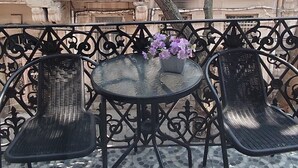 Un balcón con suelo de baldosas, una mesa redonda, dos sillas y una planta en maceta.