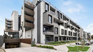 Un edifici residencial modern de diverses plantes amb balcons, entrada tancada i un jardí ben cuidat.