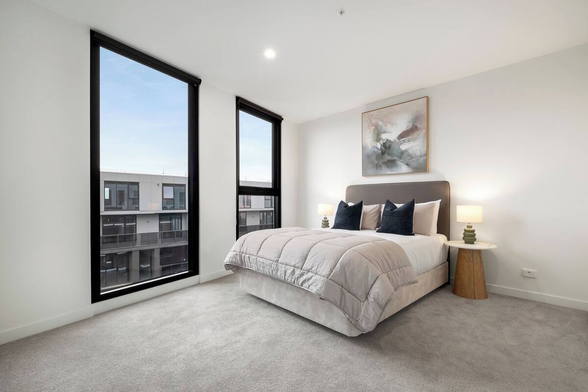 A modern bedroom with a large bed, two bedside lamps, a city view, and a painting on the wall.