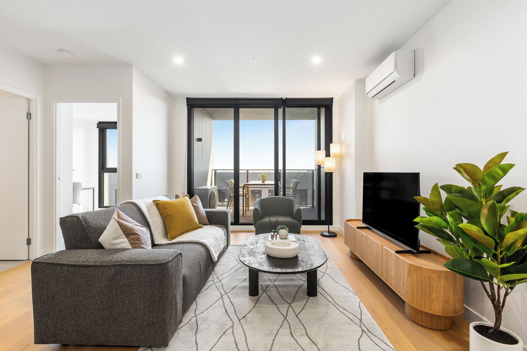 A modern living room with a sofa, a coffee table, a TV, and a balcony with outdoor furniture.