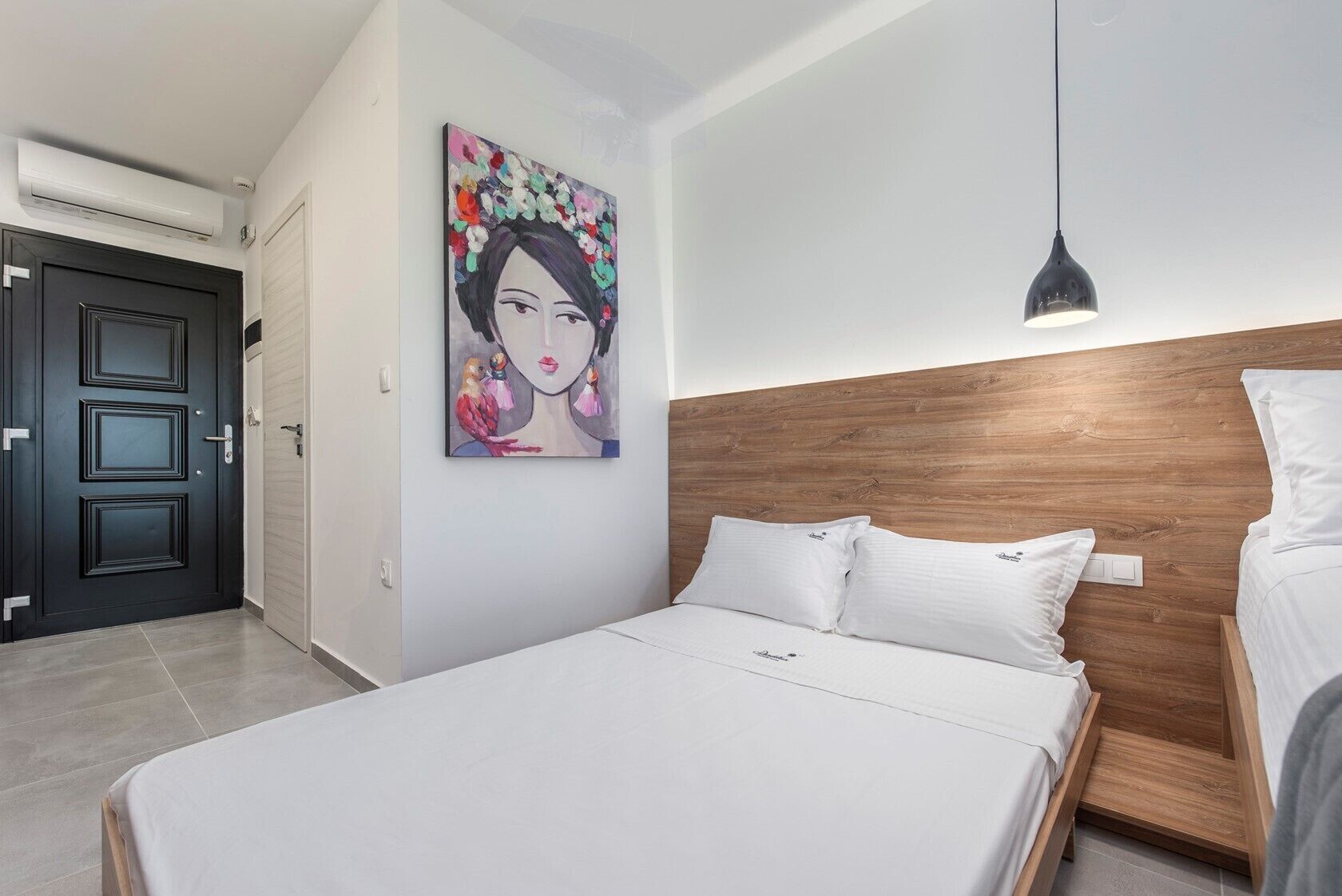 Un dormitorio moderno con cabecera de madera, una cama grande con ropa blanca, un cuadro colorido en la pared y una lámpara colgante.