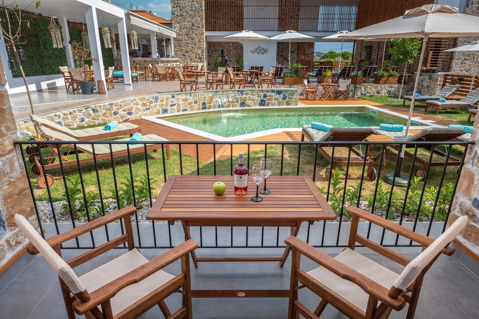 A poolside area with a table, chairs, and a bottle of wine.