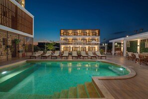 Un immeuble à plusieurs étages doté d’une piscine, d’un espace extérieur aménagé pour s’asseoir et d’une façade en pierre.
