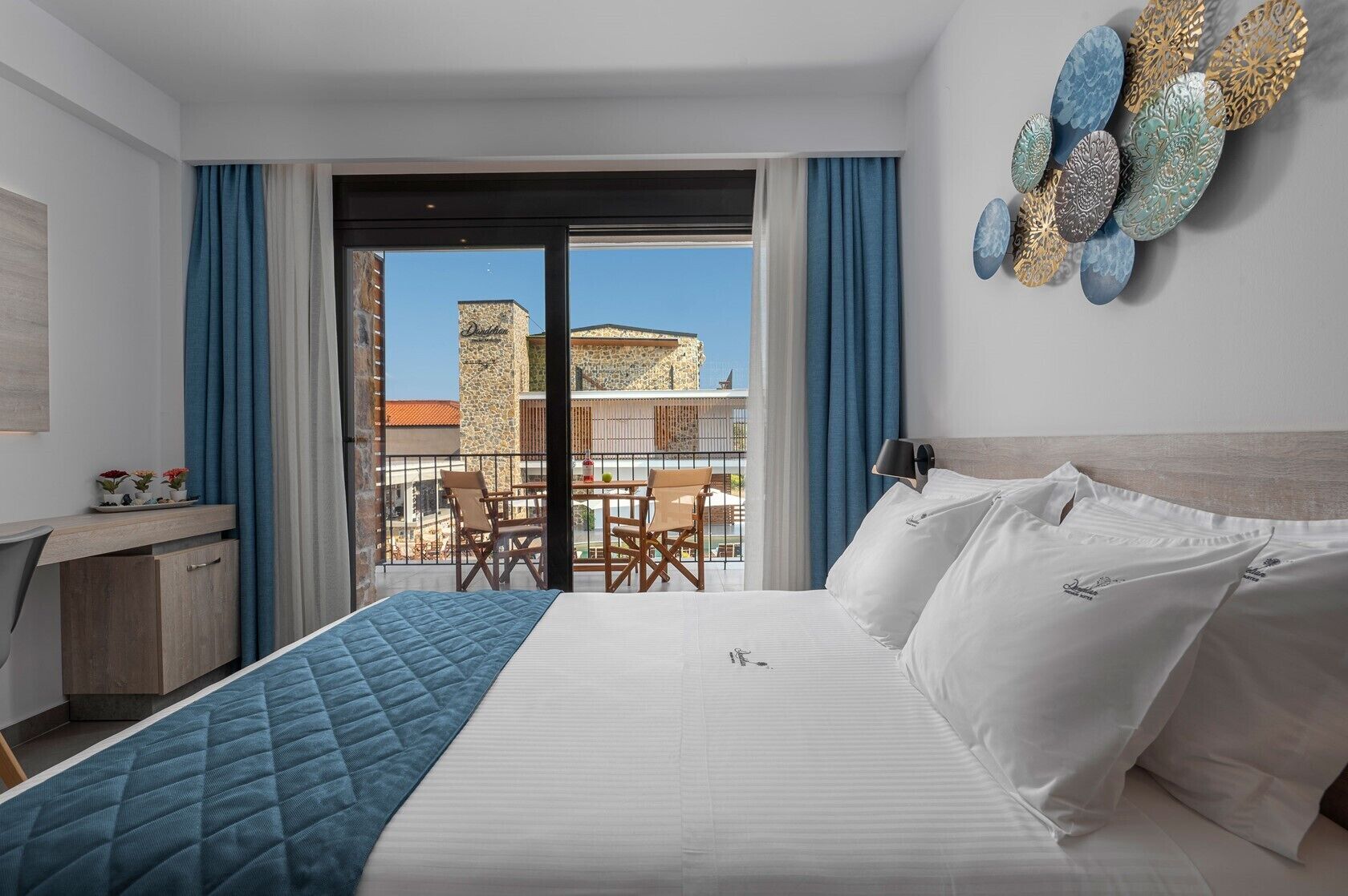 A hotel room with a bed, a desk, and a balcony with a view of buildings.