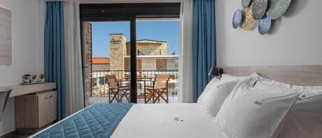 A hotel room with a bed, a desk, and a balcony with a view of buildings.