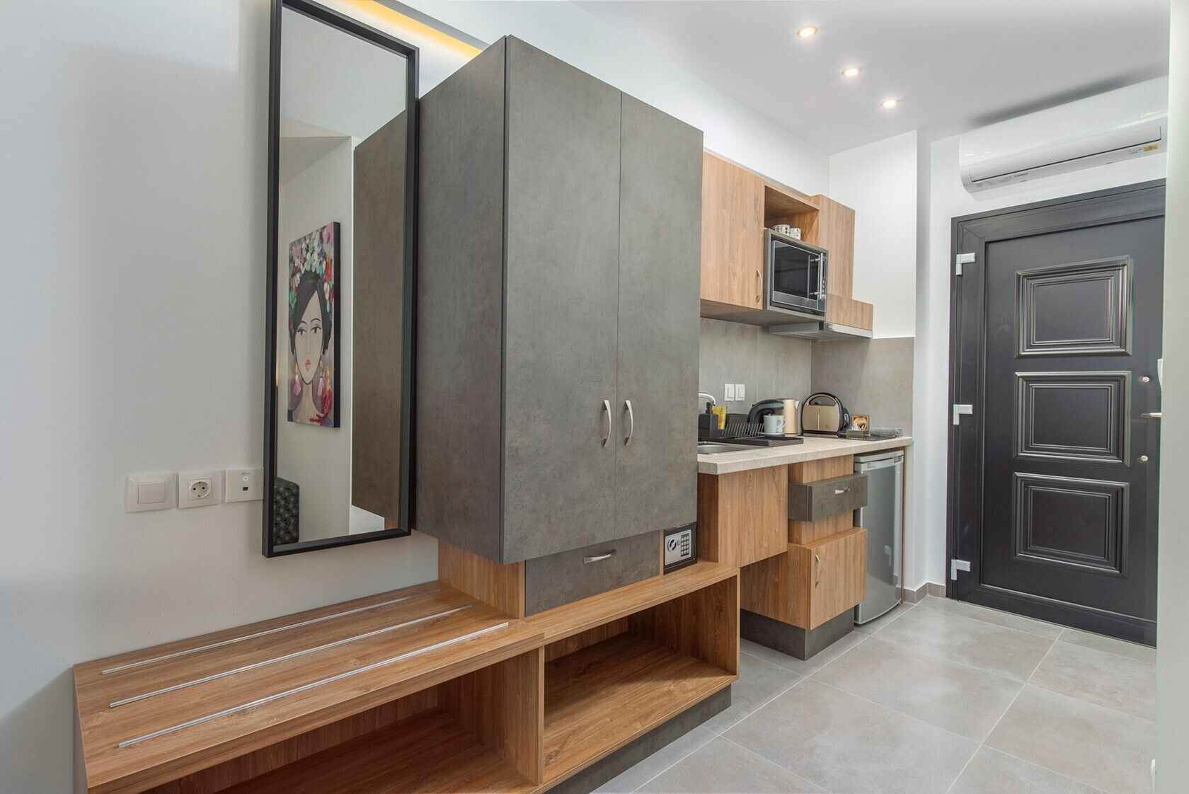 A modern kitchen with grey cabinets, wooden shelves, and a built-in microwave.