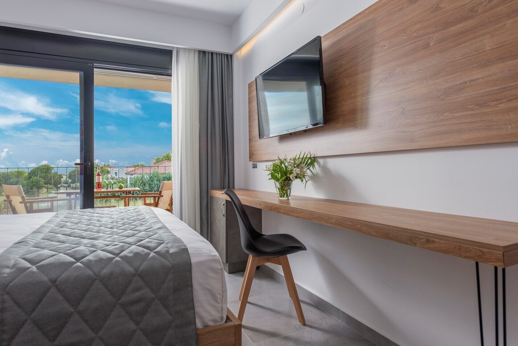 A hotel room with a bed, a desk, a chair, a TV, and a balcony with a view.