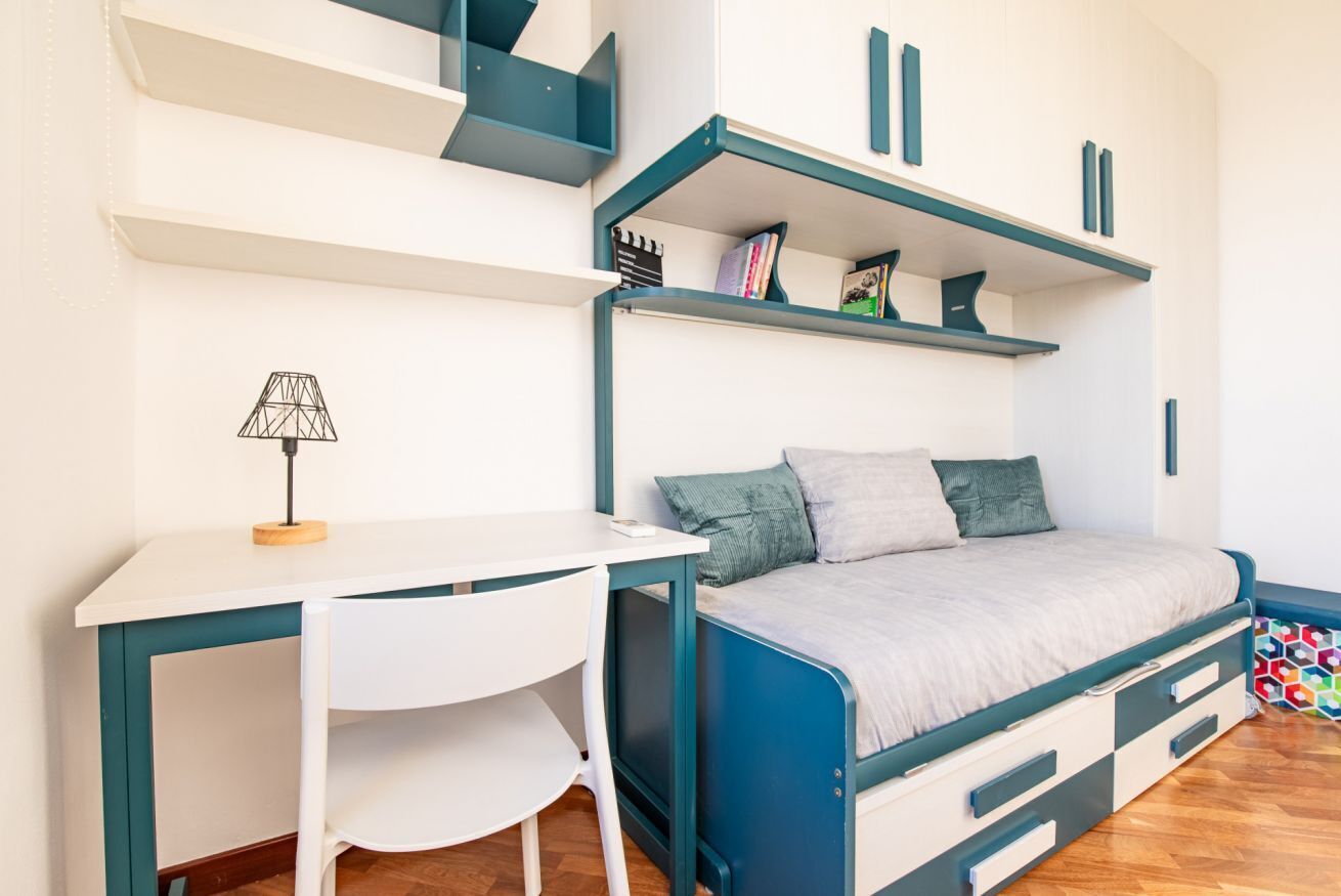 A compact bedroom with a bed, a desk, and shelving units.