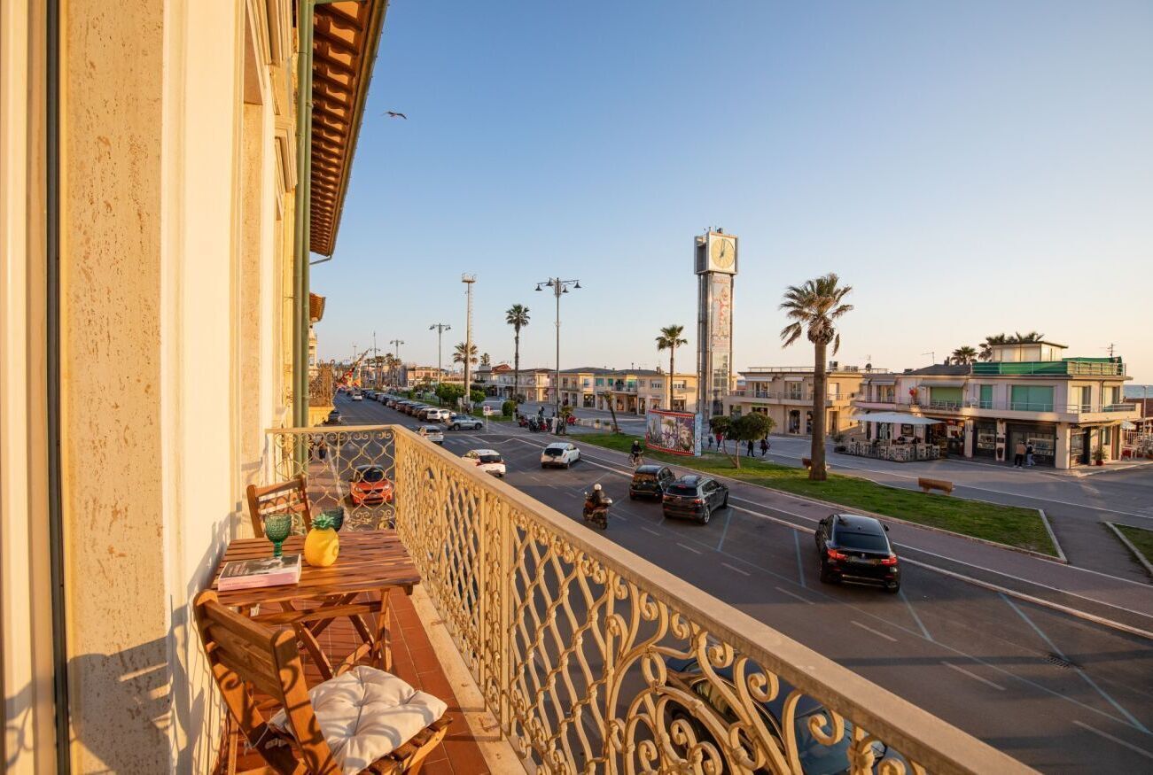 A balcony with a view of a busy street, palm trees, and a clock tower.