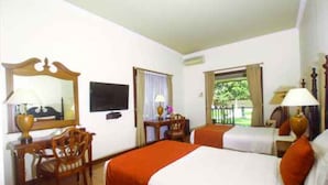 A hotel room with two beds, a desk, a chair, a television, and a window with a view of greenery. - Villa Grand Artos (Magelang)