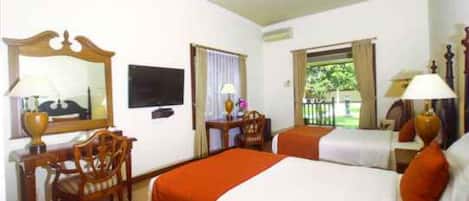 Habitación de hotel con dos camas, un escritorio, una silla, un televisor y una ventana con vistas a zonas verdes.