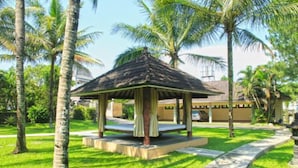 A gazebo with a thatched roof, surrounded by palm trees and a well-maintained lawn. - Villa Grand Artos (Magelang)