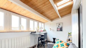 Una stanza accogliente con soffitto in legno, un divano con cuscini decorati, una scrivania e un termosifone.