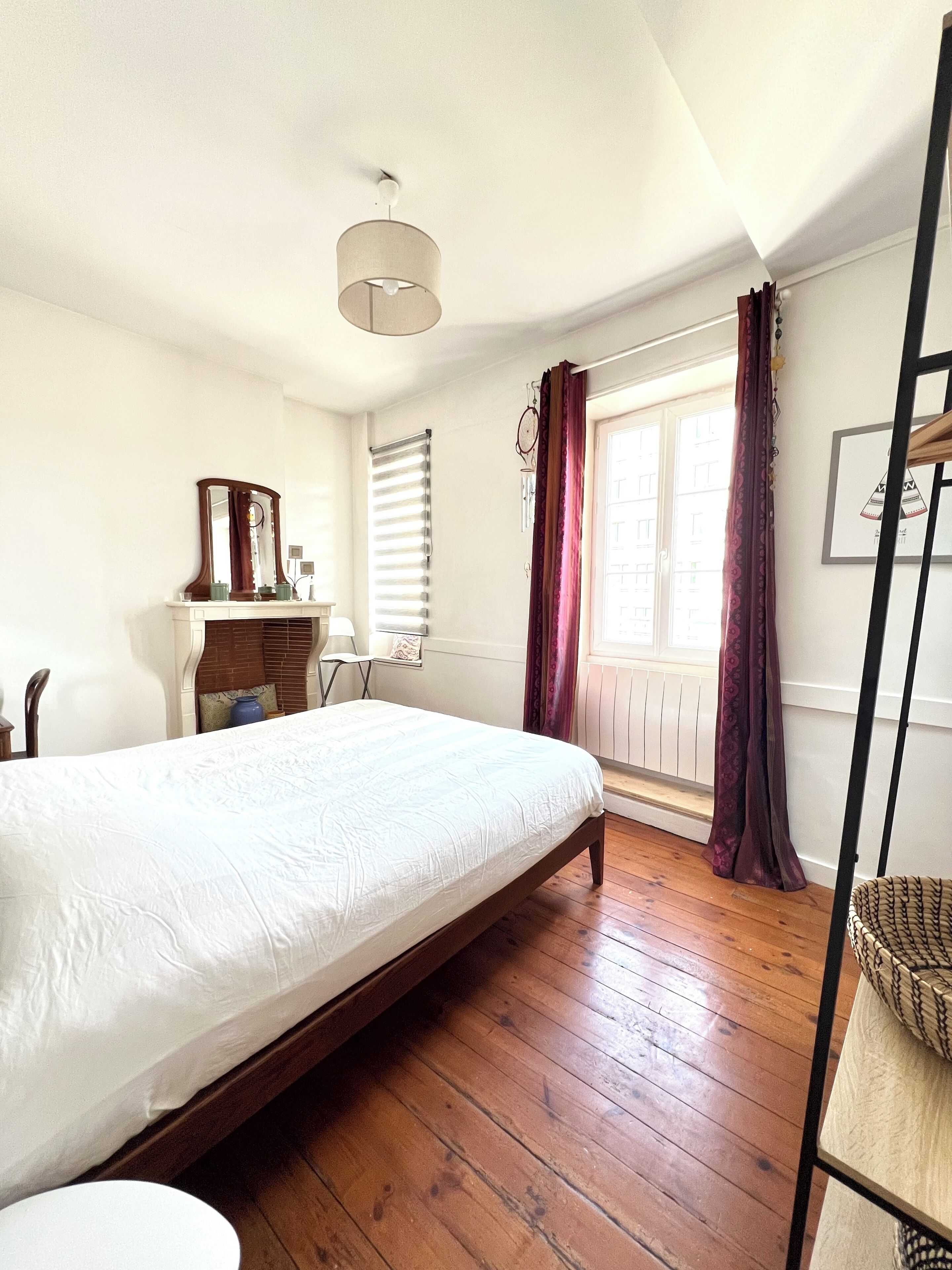 Une chambre avec un lit simple, une commode, un miroir, une fenêtre avec des rideaux et un luminaire suspendu.