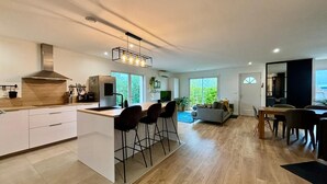 A modern kitchen with a central island, bar stools, and a dining area with a view of the outdoors.