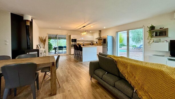 A modern living space with a dining area, kitchen, and a cozy seating area with a sofa and a yellow throw blanket.