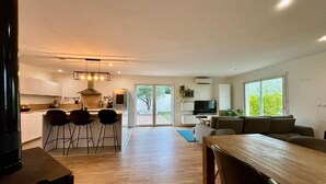 A modern kitchen with a dining area, a TV, and a large window.