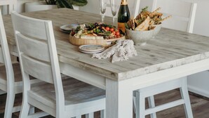Una mesa de comedor con una lámpara colgante de tejido, un cuadro con una piscina y un bol de pan y verduras.