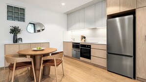 Eine moderne Küche mit Holzschränken, einem Edelstahlkühlschrank, einem runden Esstisch mit Stühlen und einem kleinen Blumentopf.
