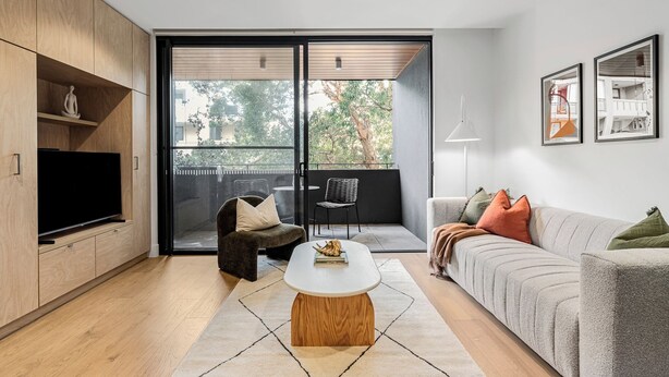 Ein modernes Wohnzimmer mit Flachbildfernseher, einer Couch, einem Couchtisch und einem Balkon mit einem Sessel.