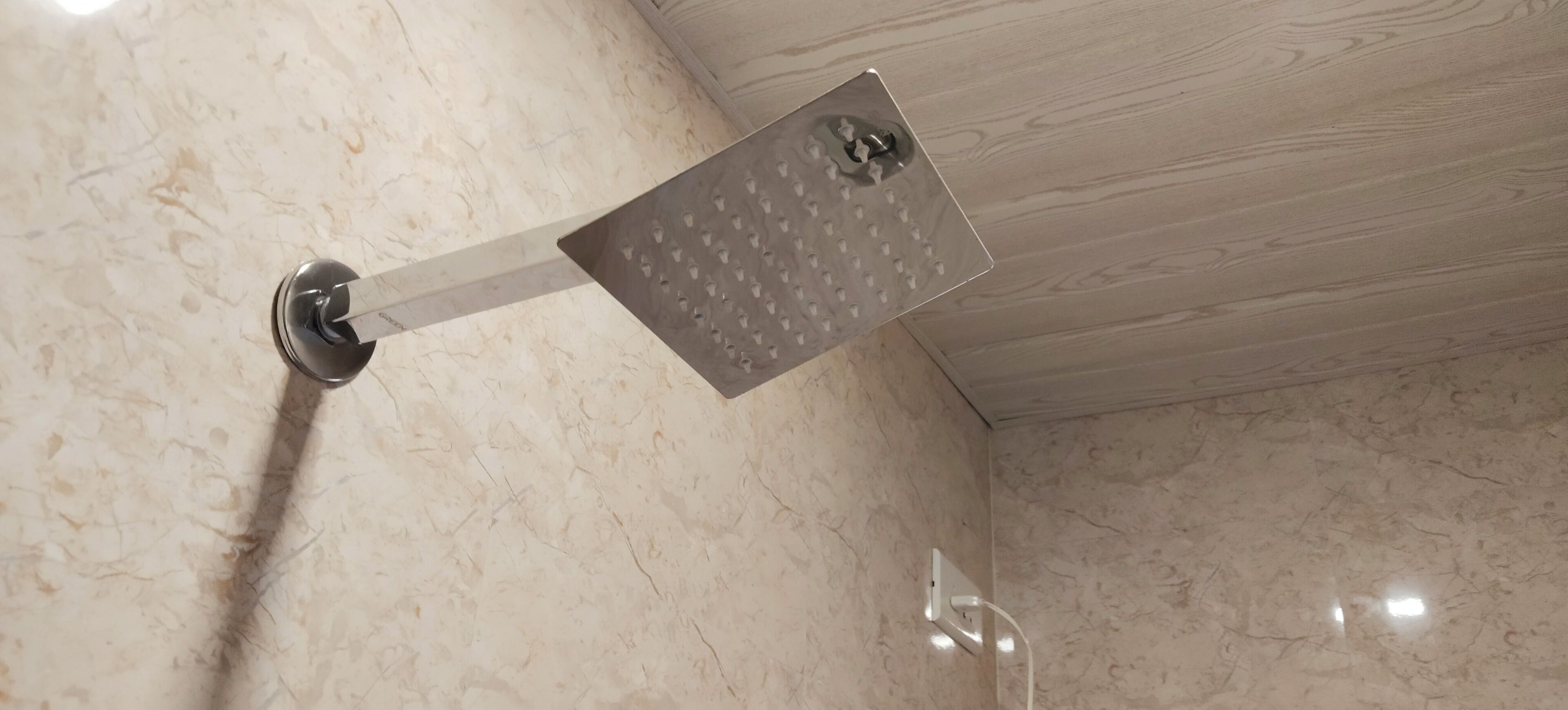 A showerhead with a perforated cover, mounted on a wall with a marble finish.