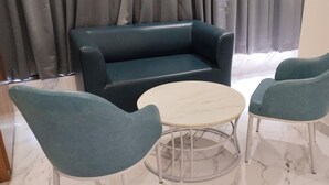 A living room with a dark blue sofa, two teal armchairs, and a small round table with a marble top. - Hotel Sai Executive (Rajgurunagar)