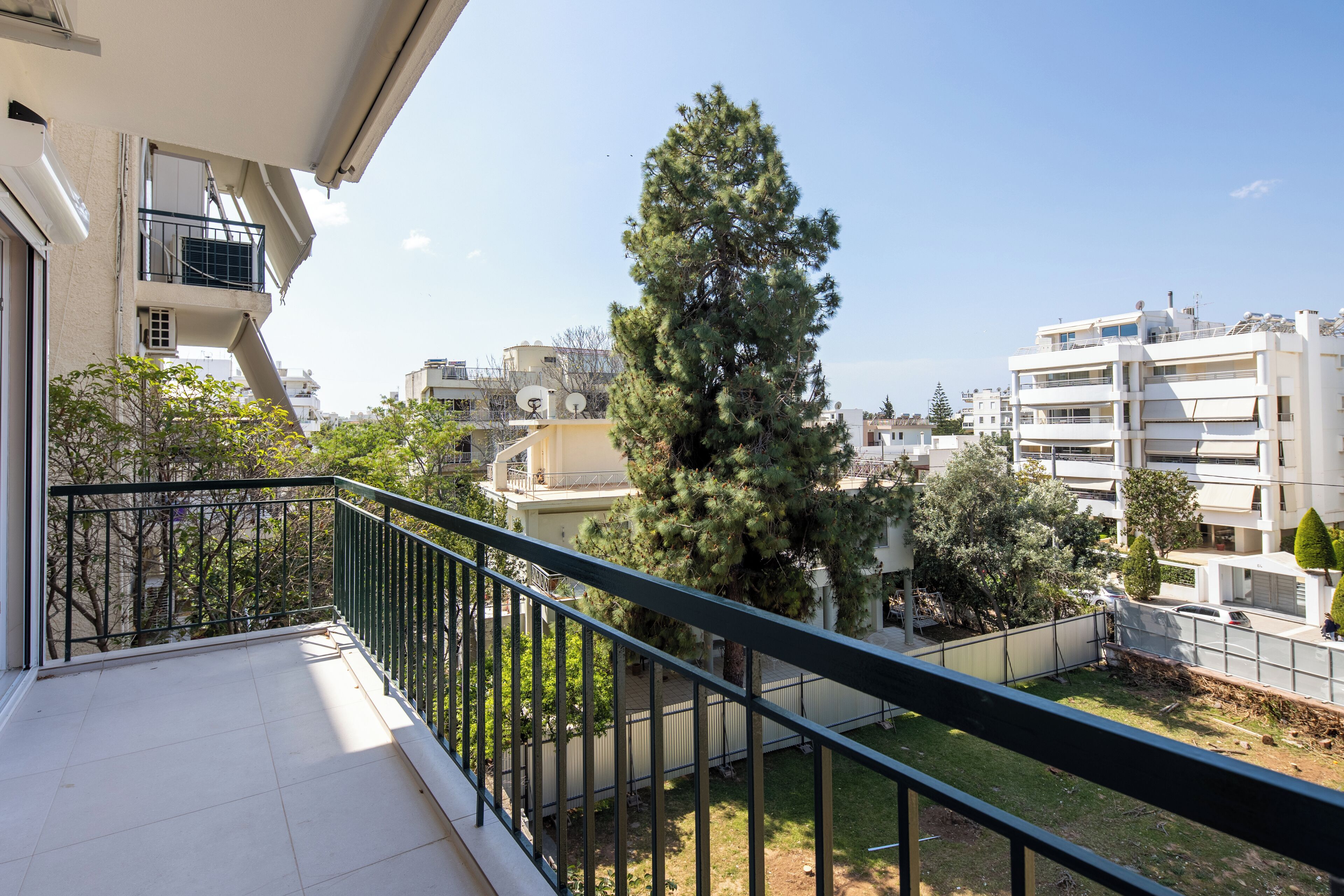 A balcony with a metal railing overlooking a residential area with trees and buildings.