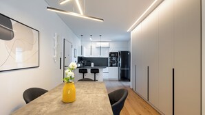 Una cocina moderna con armarios blancos, un refrigerador negro y un comedor con un jarrón amarillo y dos sillas.