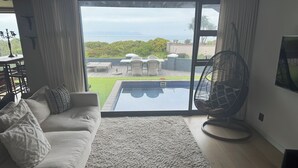 A living room with a large sliding glass door leading to a pool area, a sofa with cushions, a fan, and a TV on the wall.