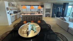 A modern kitchen with a central island, pendant lighting, and a dining area with a glass table.