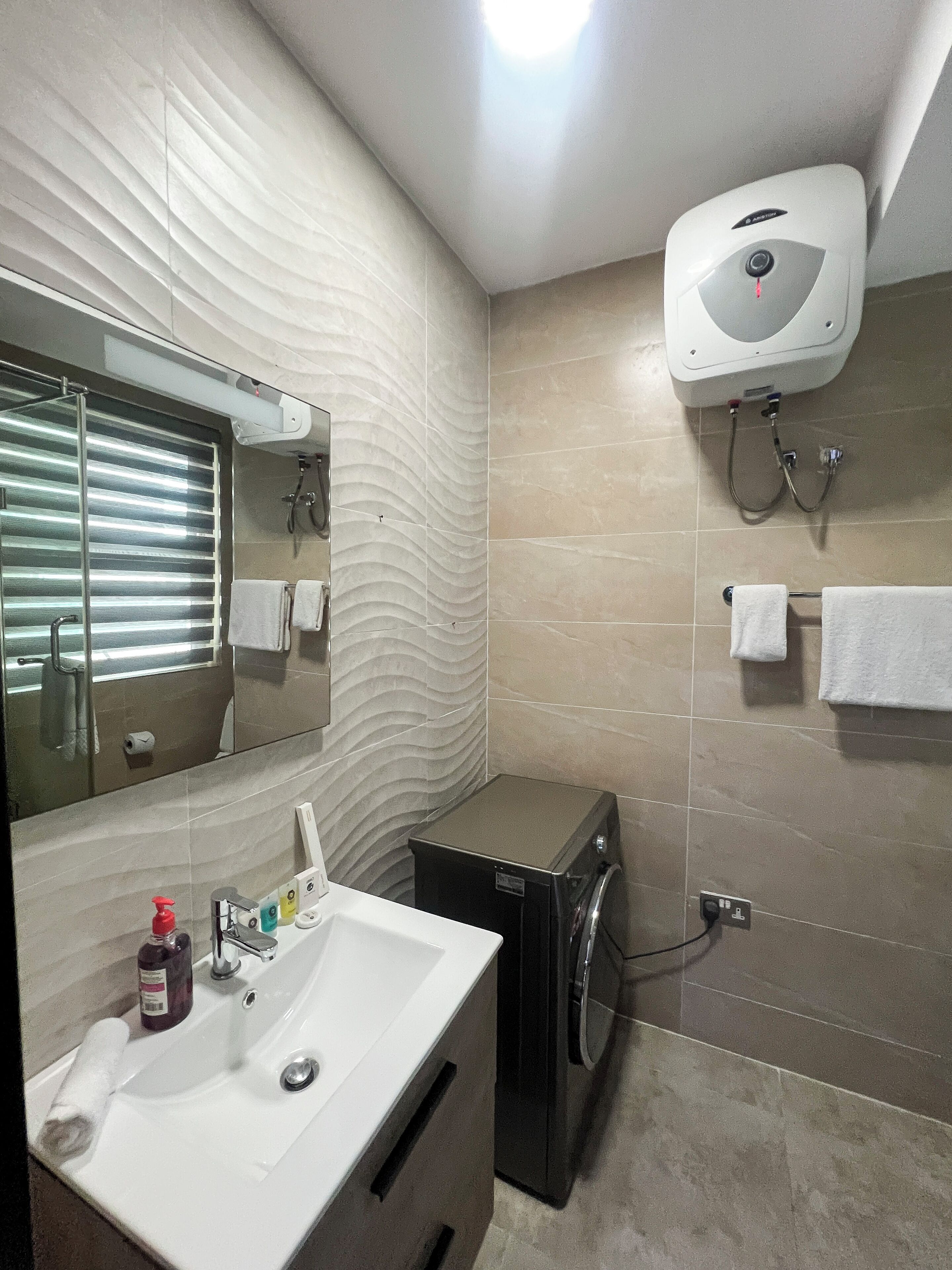 Une salle de bain moderne avec un lavabo blanc, un miroir, un porte-serviettes, une douchette à main et un sèche-mains fixé au mur.