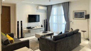 Egy modern nappali, melyben egy síkképernyős televízió, szürke színű kanapék, egy dohányzóasztal és egy étkező található.