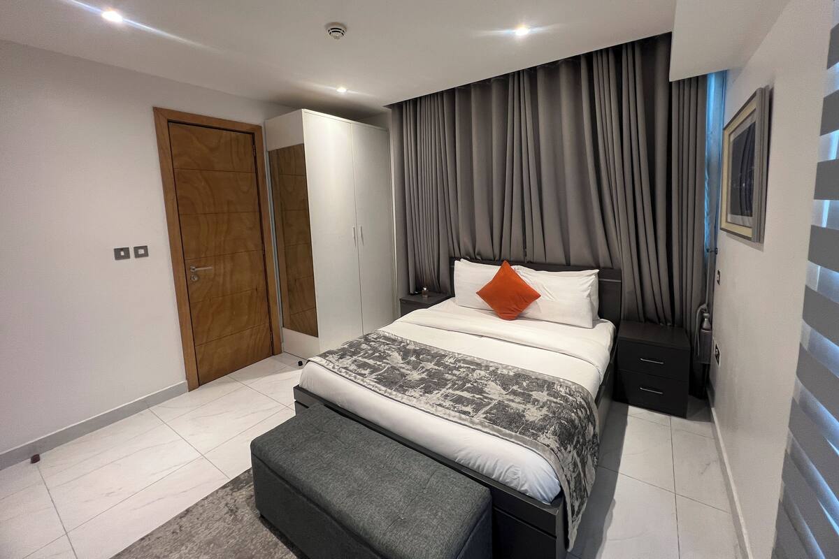 Une chambre à coucher moderne, avec un lit, une table de chevet, une armoire et une grande fenêtre avec des rideaux.