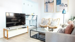 A modern living room with a flat-screen TV, wicker chairs, a glass coffee table, and abstract wall art. - Tinto Townhouse  (Seville)