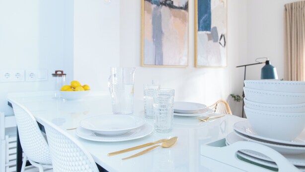 A dining table set with white plates, glasses, and cutlery, with abstract art on the wall and a lamp in the background. - Tinto Townhouse  (Seville)