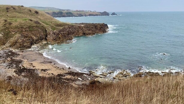 A coastal landscape with rocky cliffs, a sandy beach, and a view of the sea.