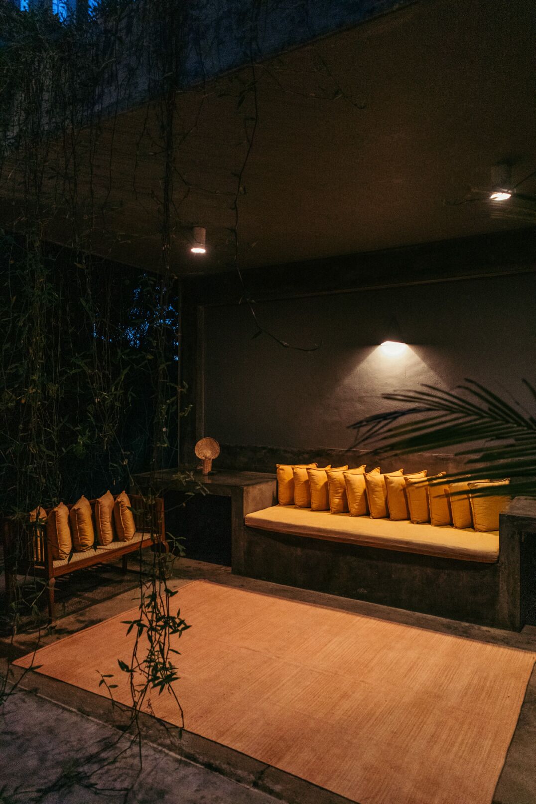 A modern outdoor seating area with a sofa and cushions, surrounded by plants and a wooden bench.