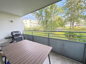 Ein Balkon mit Grill, Tisch und Blick auf ein Gebäude sowie Bäume.