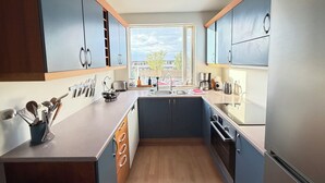 A modern kitchen with wooden cabinets, a central island, and a view of the outside. - Cosy and family friendly apartment in Kópavogur - Birta Rentals (Kópavogur)