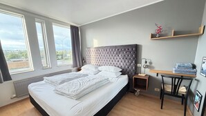 A bedroom with a large bed, a nightstand, a table with a lamp, and a view of the outside. - Cosy and family friendly apartment in Kópavogur - Birta Rentals (Kópavogur)