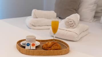 A neatly made bed with white linens and rolled towels, a tray with croissants, a glass of orange juice, and two cups of coffee.