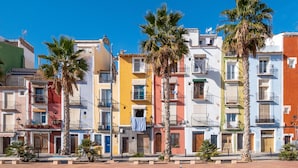 A row of colorful Mediterranean-style buildings with balconies, palm trees, and a clear blue sky. - Lucentina Line (Villajoyosa)